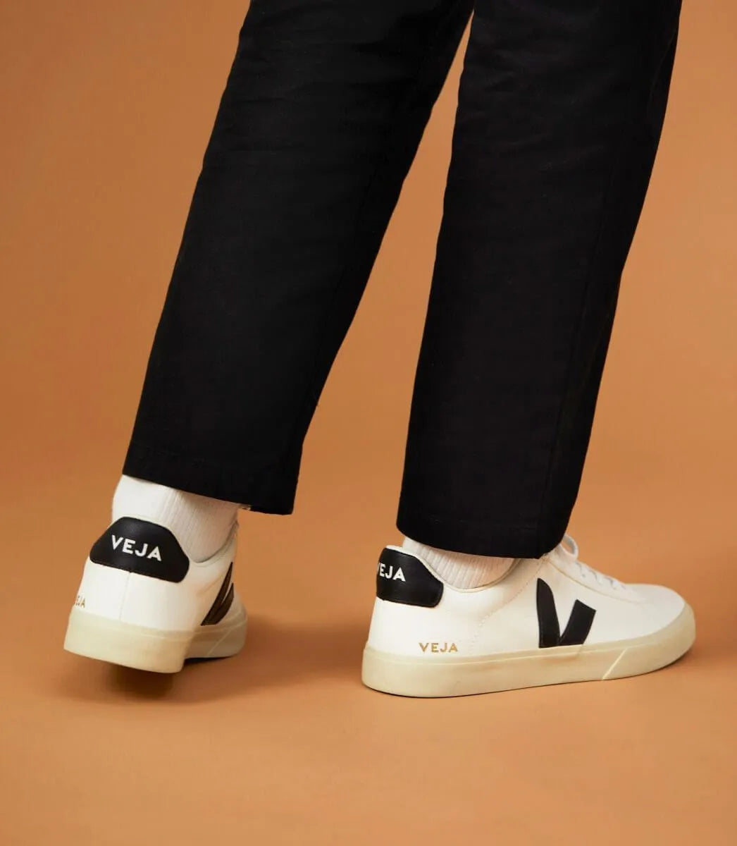 White and black Veja Campo sneakers worn with black pants on a brown background